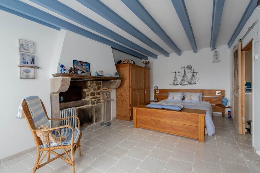 Réalisation d'une chambre d'amis méditerranéenne de taille moyenne avec un mur blanc, un sol en carrelage de céramique, une cheminée standard, un manteau de cheminée en pierre et un sol beige.