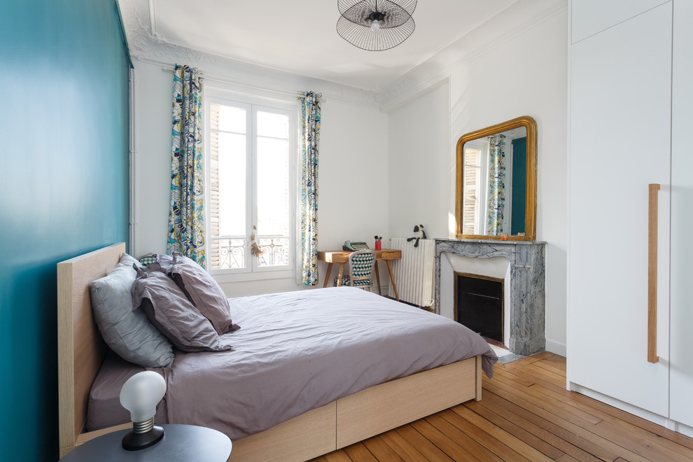 Modelo de dormitorio principal escandinavo de tamaño medio con paredes azules, suelo de madera en tonos medios, todas las chimeneas, marco de chimenea de piedra y suelo marrón
