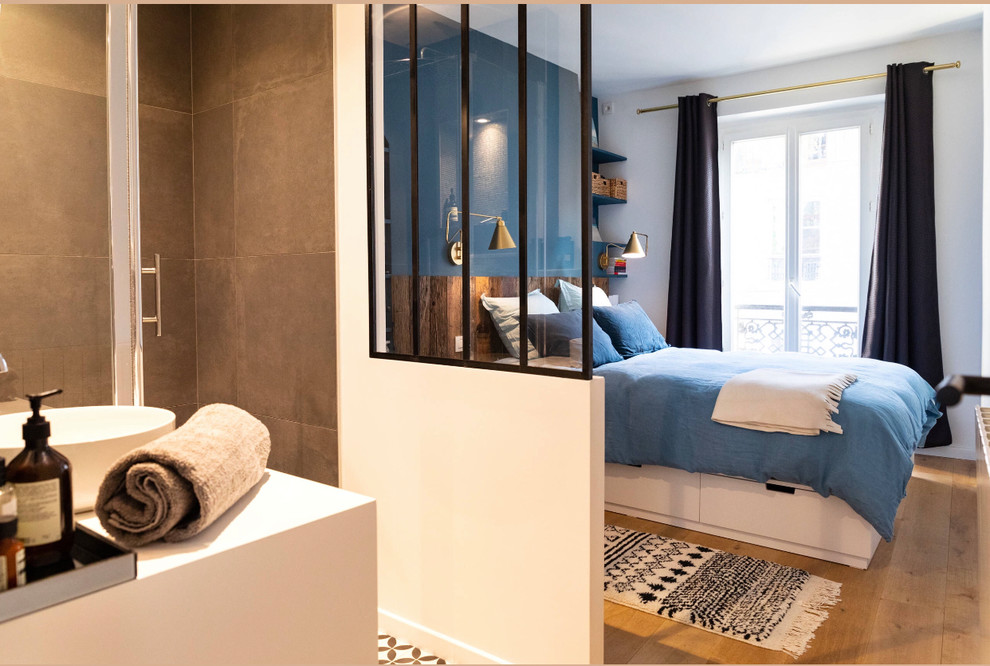 Diseño de dormitorio principal minimalista pequeño sin chimenea con paredes azules, suelo de madera clara y suelo marrón
