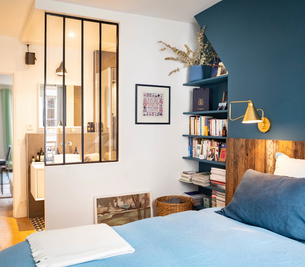 Modelo de dormitorio principal moderno pequeño sin chimenea con paredes azules, suelo de madera clara y suelo marrón