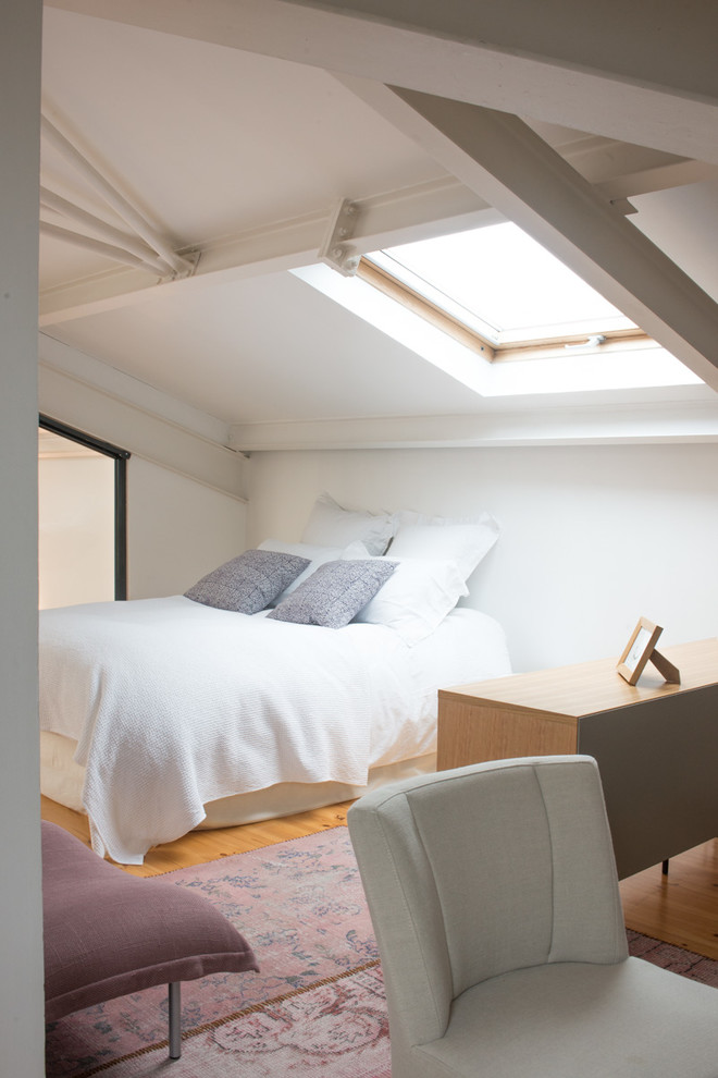 Exemple d'une chambre mansardée ou avec mezzanine chic de taille moyenne avec un mur blanc et un sol en bois brun.