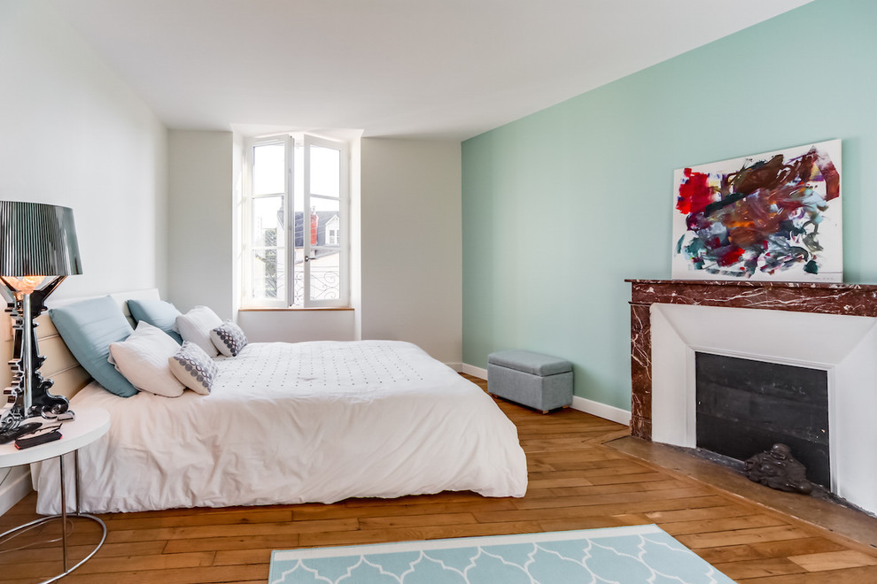 Inspiration pour une chambre parentale design de taille moyenne avec un mur bleu, parquet clair, une cheminée standard, un manteau de cheminée en pierre et un sol marron.