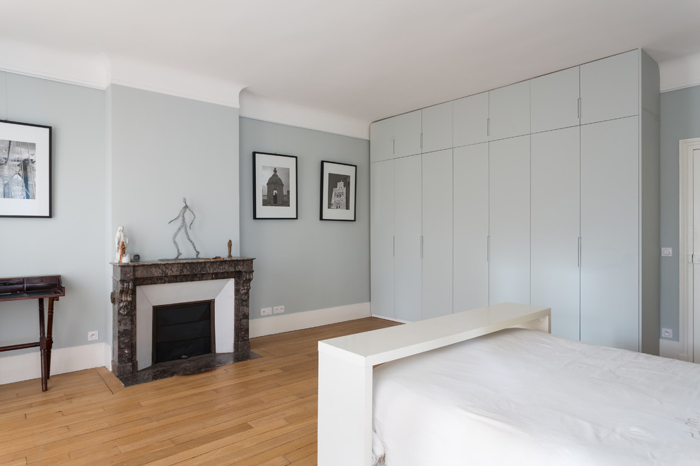 Großes Modernes Hauptschlafzimmer mit braunem Holzboden, Kamin, beigem Boden, grauer Wandfarbe und Kaminumrandung aus Stein in Paris