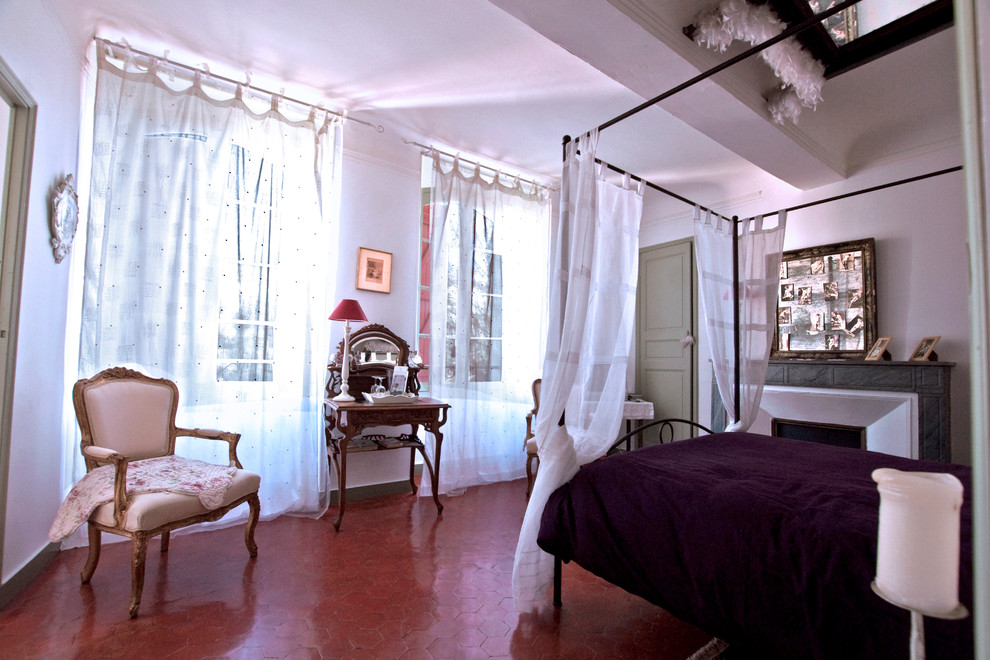 На фото: хозяйская спальня среднего размера в стиле шебби-шик с белыми стенами, полом из терракотовой плитки, стандартным камином, фасадом камина из камня и красным полом