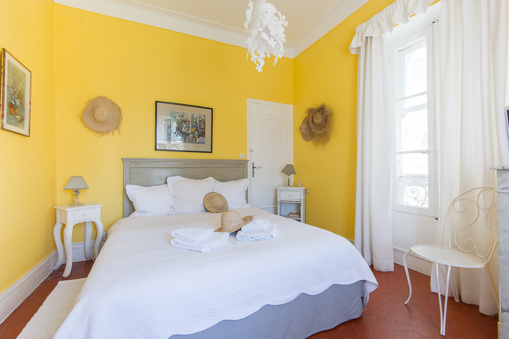 Aménagement d'une grande chambre d'amis méditerranéenne avec un mur jaune et tomettes au sol.