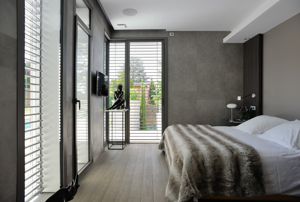 Cette photo montre une chambre parentale tendance de taille moyenne avec un mur gris et un sol en bois brun.