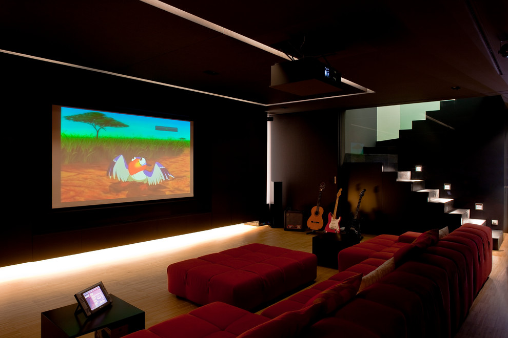 Inspiration pour une grande salle de cinéma traditionnelle ouverte avec un mur noir, un sol en bois brun et un écran de projection.