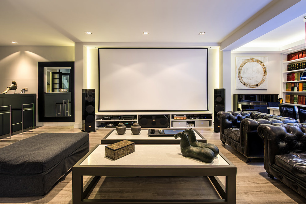 This is an example of a large modern open plan home cinema in Madrid with white walls, medium hardwood flooring and a projector screen.