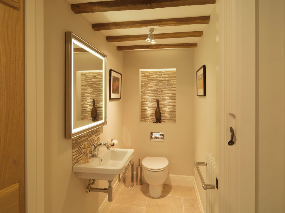 Example of a small cottage beige tile and glass tile limestone floor powder room design in Hampshire with a wall-mount sink, beige walls and a one-piece toilet