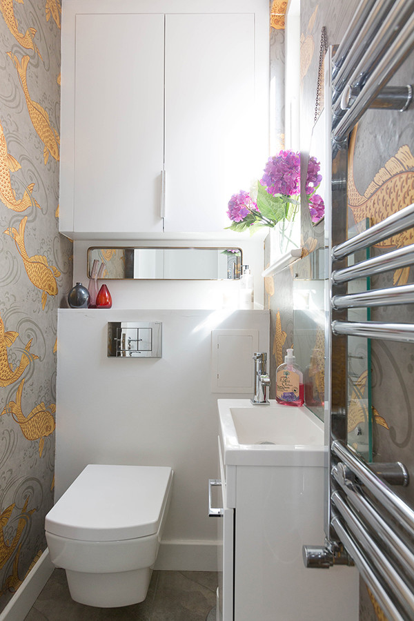 Idée de décoration pour un petit WC suspendu design avec un placard à porte plane, des portes de placard blanches, un mur multicolore et un lavabo intégré.