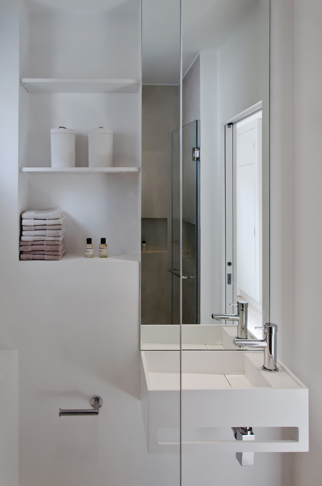 Modern inredning av ett stort toalett, med släta luckor, grå skåp, en vägghängd toalettstol, beige kakel, keramikplattor, vita väggar, klinkergolv i keramik, ett väggmonterat handfat och grått golv