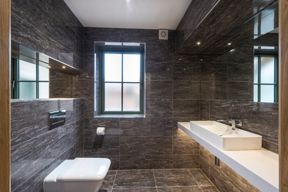 Идея дизайна: большой туалет в современном стиле с инсталляцией, серой плиткой, керамогранитной плиткой, серыми стенами, полом из керамогранита, консольной раковиной, столешницей из искусственного камня, серым полом и белой столешницей