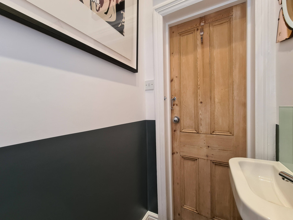 This is an example of a medium sized modern cloakroom in London with freestanding cabinets, white cabinets, a two-piece toilet, porcelain tiles, white walls, porcelain flooring, a wall-mounted sink, beige floors, a freestanding vanity unit and a drop ceiling.