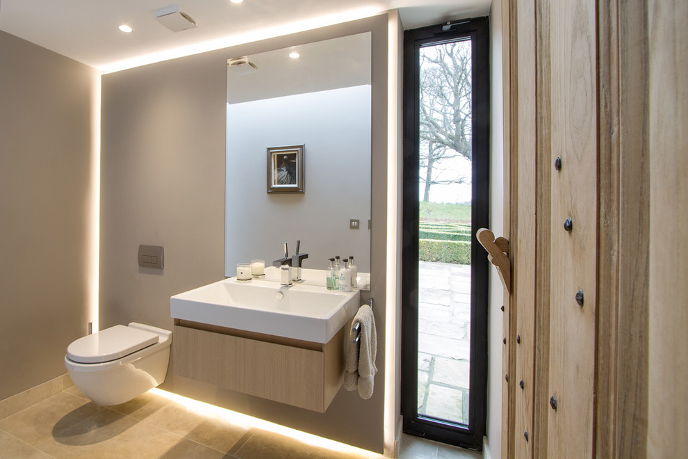 Idee per un bagno di servizio design di medie dimensioni con ante lisce, ante in legno chiaro, WC sospeso, pareti beige, pavimento in pietra calcarea, lavabo sospeso e pavimento beige