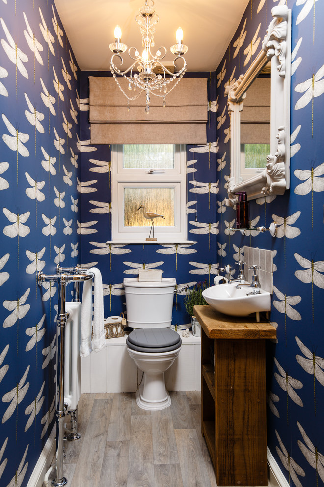 This is an example of a bohemian cloakroom in Cambridgeshire with freestanding cabinets, dark wood cabinets, blue walls, laminate floors, a wall-mounted sink, wooden worktops, a two-piece toilet, grey tiles, grey floors and brown worktops.