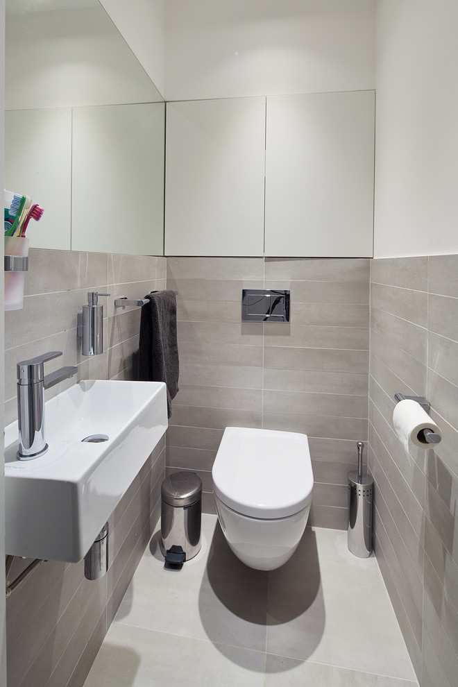 Small contemporary cloakroom in London with flat-panel cabinets, white cabinets, a wall mounted toilet, grey tiles, porcelain tiles, grey walls, porcelain flooring, a wall-mounted sink, tiled worktops, grey floors and grey worktops.
