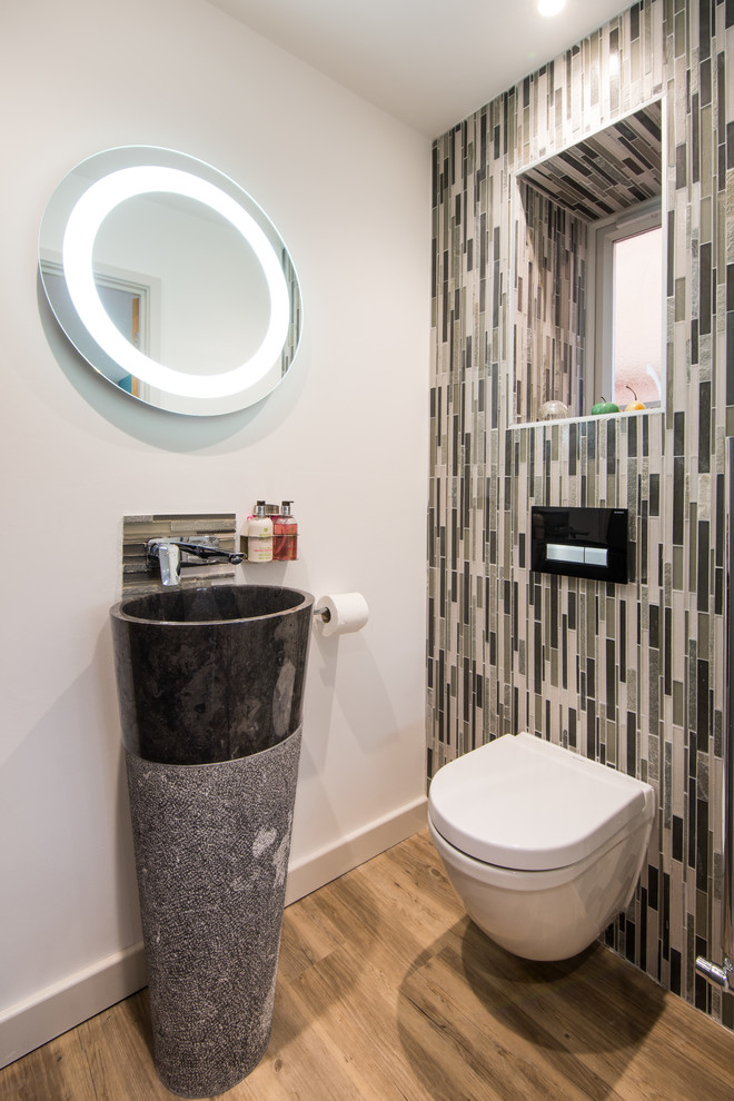 Inspiration for a small modern cloakroom in West Midlands with a wall mounted toilet, multi-coloured tiles, matchstick tiles, beige walls, medium hardwood flooring, a pedestal sink and brown floors.