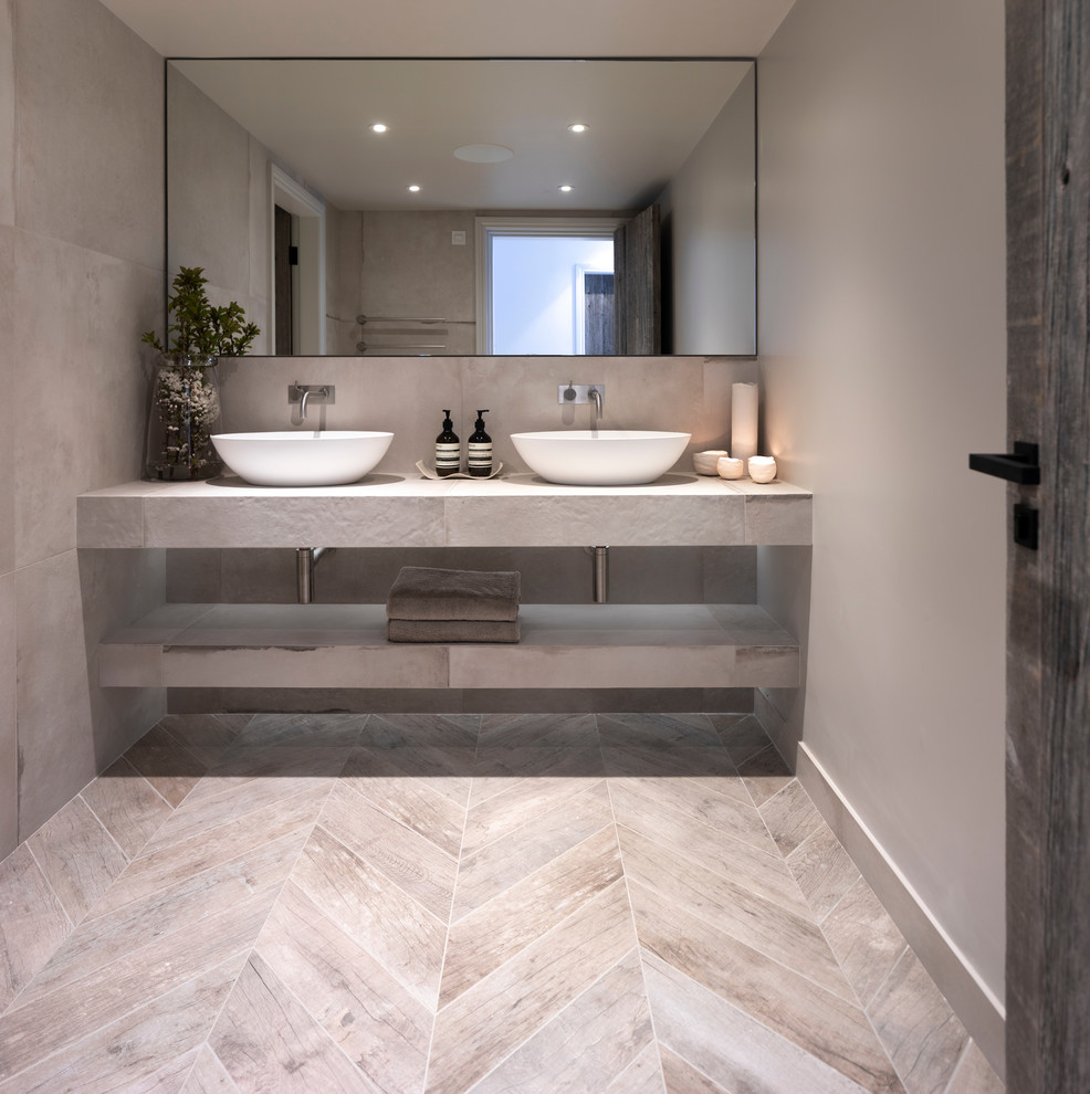 Design ideas for a medium sized contemporary cloakroom in Cheshire with a wall mounted toilet, grey tiles, porcelain tiles, grey walls, porcelain flooring, a trough sink, tiled worktops, grey floors and grey worktops.