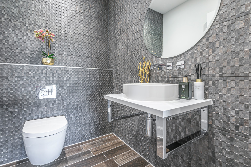 Immagine di un bagno di servizio contemporaneo con WC sospeso, piastrelle grigie, lavabo a bacinella, pavimento marrone e top bianco