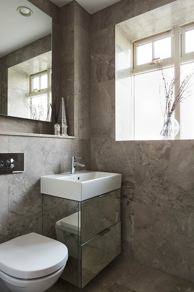 На фото: туалет в современном стиле с плоскими фасадами, плиткой из известняка, серой плиткой, настольной раковиной и серым полом