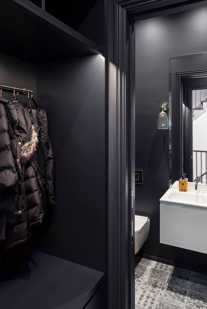 Inspiration for a small contemporary cloakroom in London with flat-panel cabinets, white cabinets, a wall mounted toilet, grey tiles, black walls, a wall-mounted sink and cement flooring.