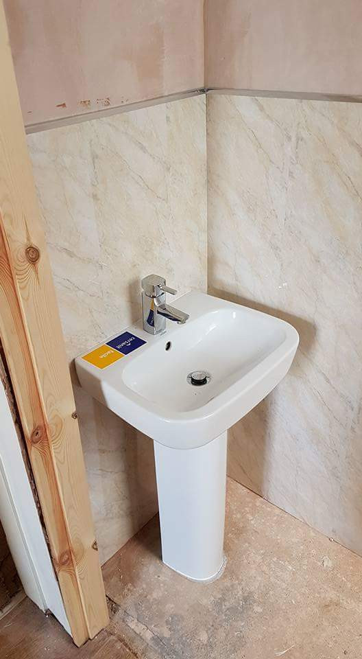 Foto på ett litet medelhavsstil toalett, med en toalettstol med hel cisternkåpa, beige kakel, travertinkakel, vita väggar, vinylgolv, ett piedestal handfat och grått golv
