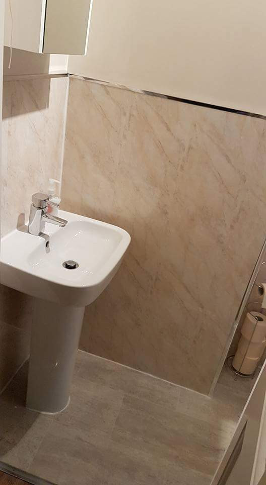 Photo of a small mediterranean cloakroom in Other with a one-piece toilet, beige tiles, travertine tiles, white walls, vinyl flooring, a pedestal sink, grey floors, a freestanding vanity unit and panelled walls.