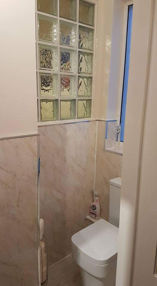 Cette image montre un petit WC et toilettes méditerranéen avec WC à poser, un carrelage beige, du carrelage en travertin, un mur blanc, un sol en vinyl, un lavabo de ferme, un sol gris, meuble-lavabo sur pied et du lambris.