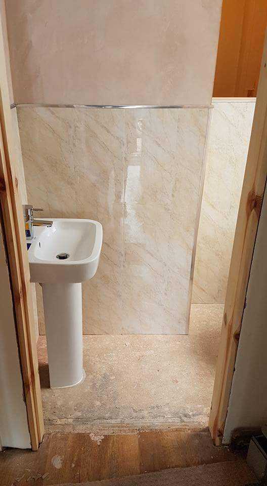 他の地域にある小さな地中海スタイルのおしゃれなトイレ・洗面所 (一体型トイレ	、ベージュのタイル、トラバーチンタイル、白い壁、クッションフロア、ペデスタルシンク、グレーの床、独立型洗面台、パネル壁) の写真