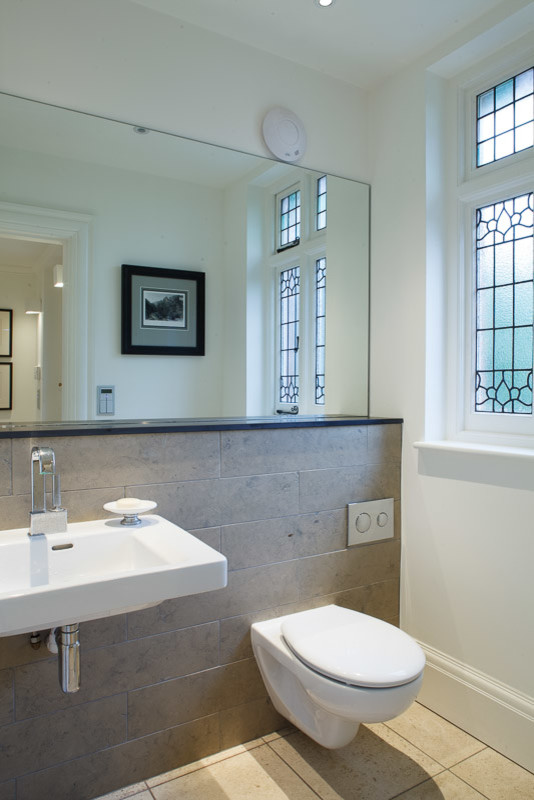Modern inredning av ett toalett, med en vägghängd toalettstol, grå kakel, vita väggar, ett väggmonterat handfat och kakelplattor