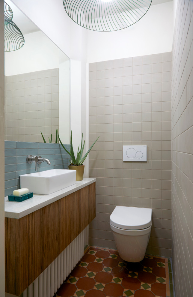 Idéer för funkis vitt toaletter, med släta luckor, skåp i mellenmörkt trä, en vägghängd toalettstol, grå kakel, vita väggar, ett fristående handfat och rött golv
