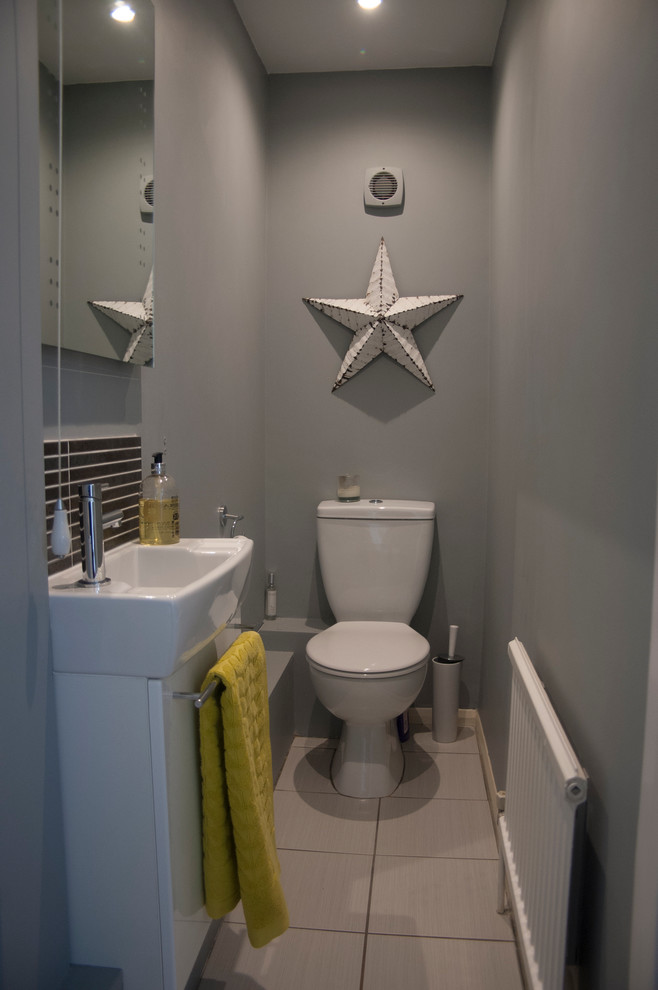 Inspiration for a small contemporary cloakroom in Berkshire with a wall-mounted sink, white cabinets, a one-piece toilet, grey walls, ceramic flooring and beige tiles.