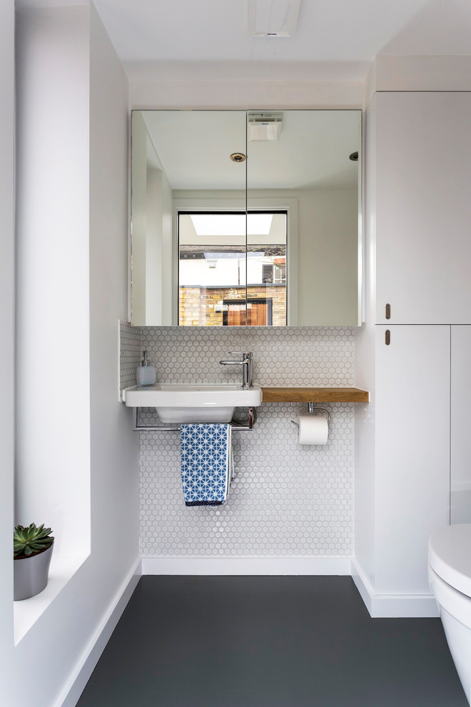 Réalisation d'un petit WC suspendu design avec un placard à porte vitrée, des carreaux de céramique, un mur blanc, un sol en vinyl, un lavabo posé, un plan de toilette en bois et un sol gris.
