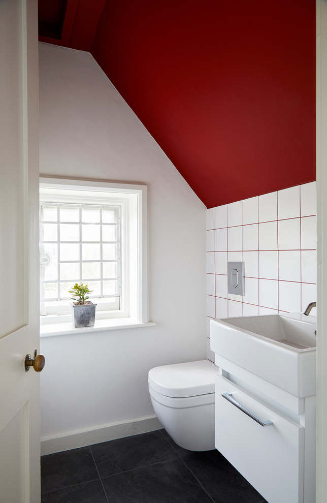Moderne Gästetoilette mit flächenbündigen Schrankfronten, weißen Schränken, weißen Fliesen, weißer Wandfarbe, Waschtischkonsole und schwarzem Boden in Surrey