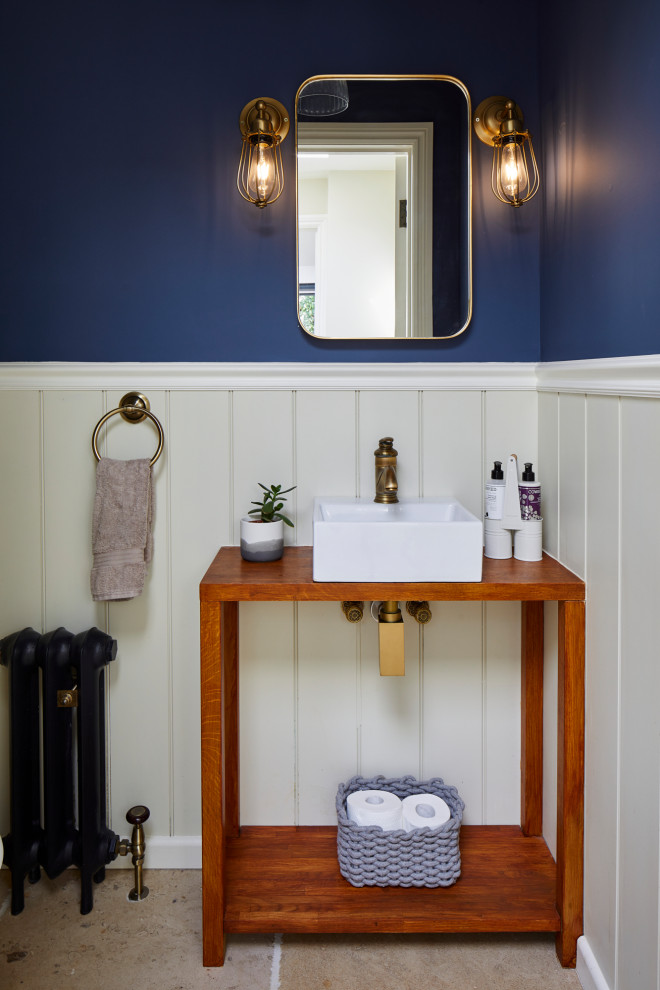 ロンドンにあるお手頃価格の小さなトラディショナルスタイルのおしゃれなトイレ・洗面所 (オープンシェルフ、茶色いキャビネット、白いタイル、青い壁、トラバーチンの床、ベッセル式洗面器、木製洗面台、ベージュの床、ブラウンの洗面カウンター、アクセントウォール、羽目板の壁、白い天井) の写真