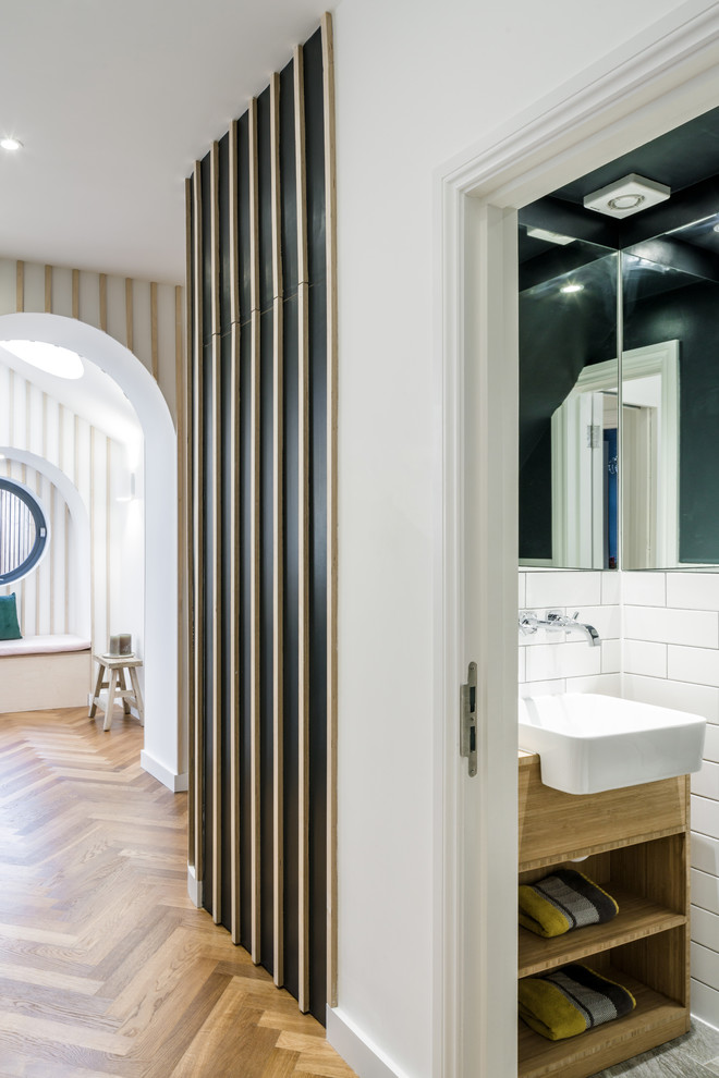 Photo of a small classic cloakroom in London with flat-panel cabinets, light wood cabinets, a wall mounted toilet, white tiles, metro tiles, grey walls, ceramic flooring, an integrated sink, wooden worktops and grey floors.