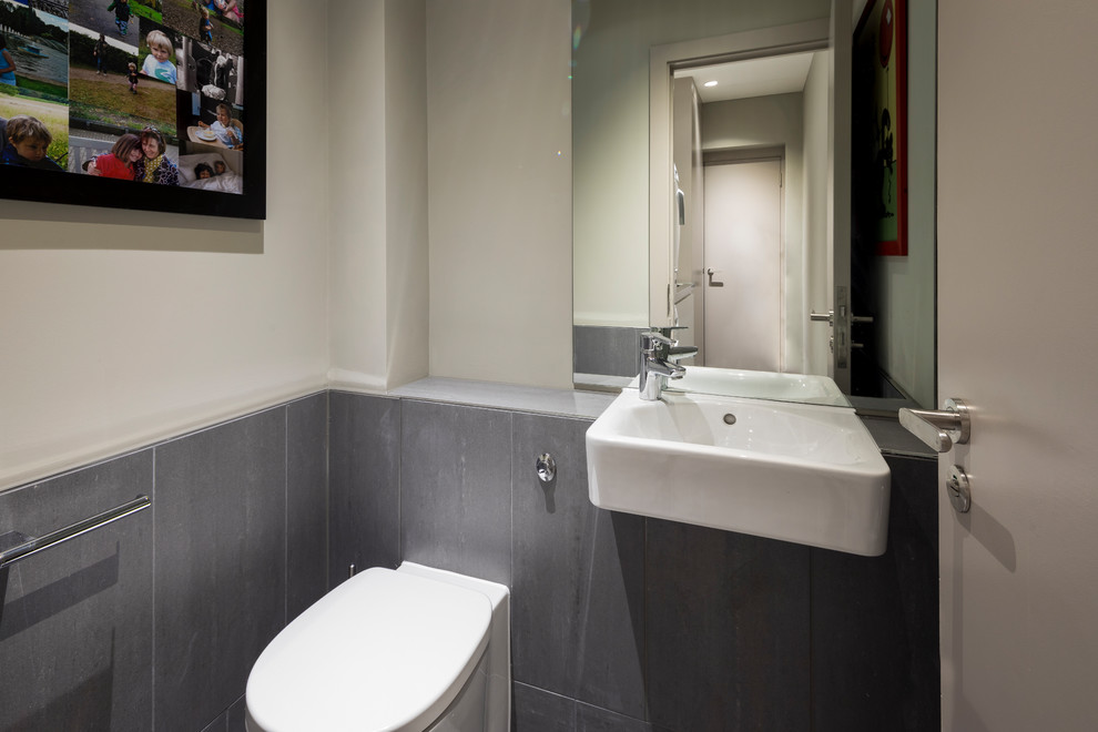 Cette photo montre un petit WC et toilettes tendance avec un carrelage gris, des carreaux de porcelaine, un mur gris, un sol en carrelage de porcelaine, un plan de toilette en carrelage et un sol gris.