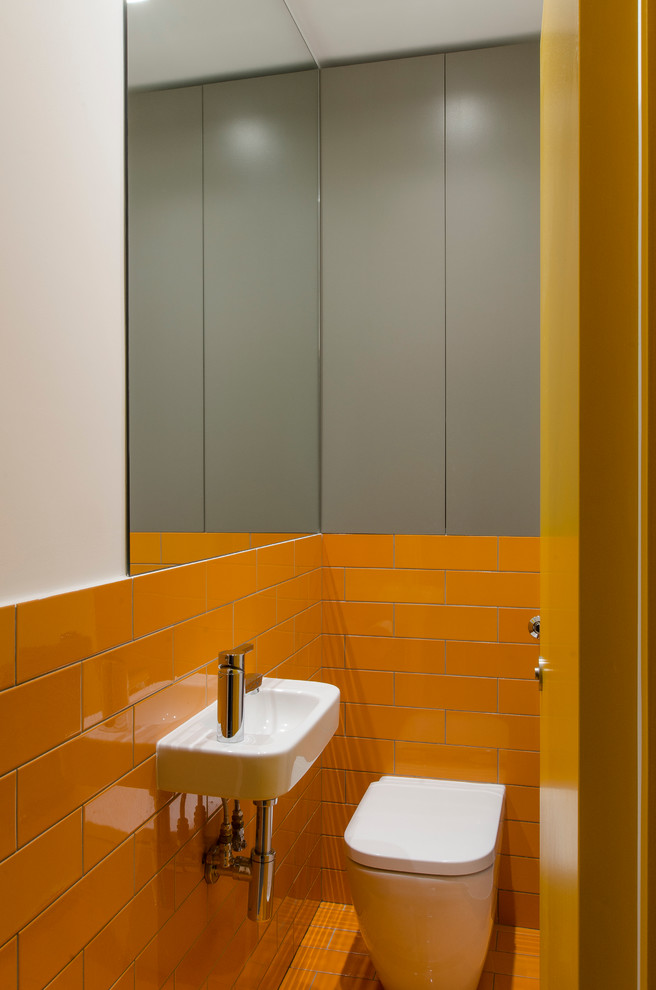 Modern inredning av ett litet toalett, med släta luckor, grå skåp, en vägghängd toalettstol, orange kakel, keramikplattor, orange väggar, klinkergolv i keramik och ett väggmonterat handfat