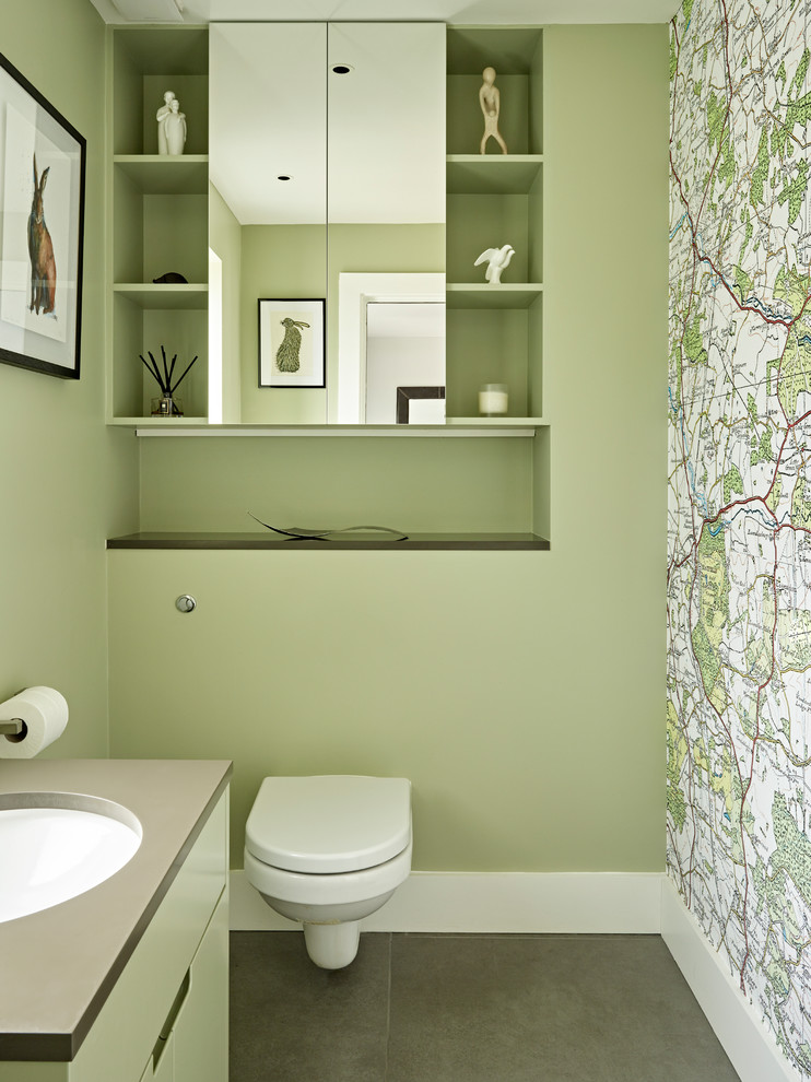 Inspiration for a contemporary cloakroom in London with flat-panel cabinets, green cabinets, a wall mounted toilet, green walls, a submerged sink, grey floors and grey worktops.