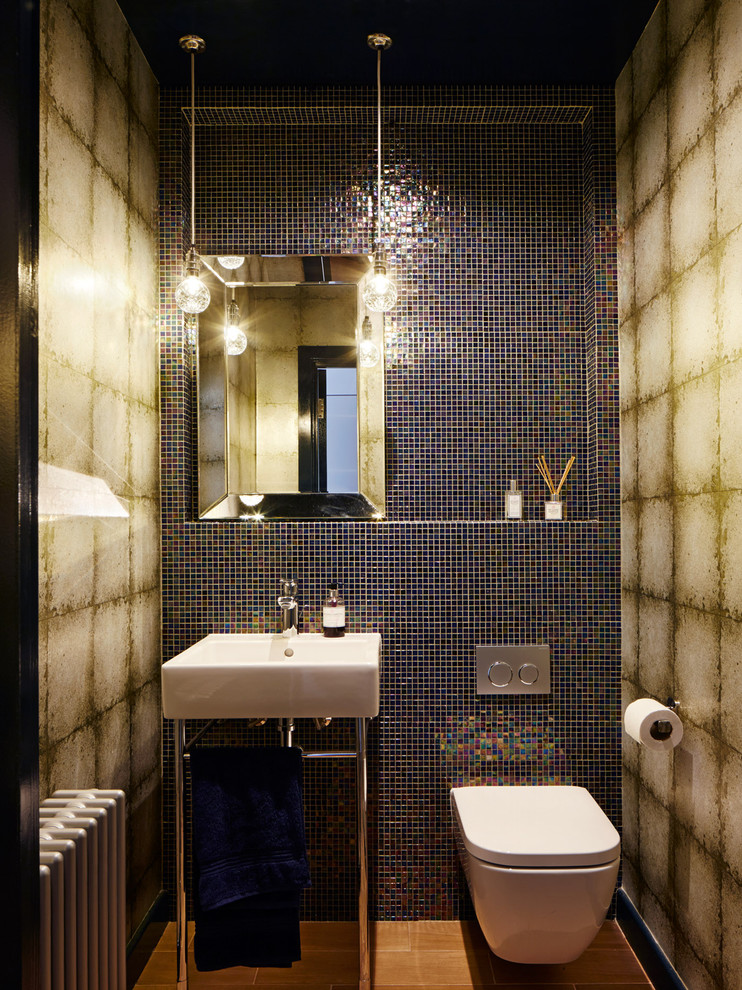 Small bohemian cloakroom in London with a wall mounted toilet, multi-coloured tiles, mosaic tiles, multi-coloured walls, a console sink, brown floors and a feature wall.