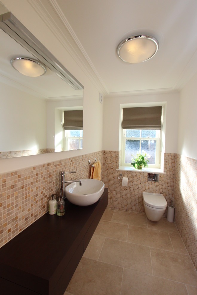 Example of a trendy beige tile powder room design in Channel Islands with wood countertops, a one-piece toilet, beige walls, a vessel sink and brown countertops