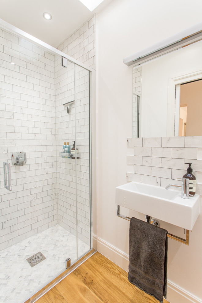 他の地域にあるお手頃価格の小さなコンテンポラリースタイルのおしゃれな浴室 (壁掛け式トイレ、セラミックタイル、白い壁、無垢フローリング、壁付け型シンク、白いタイル) の写真