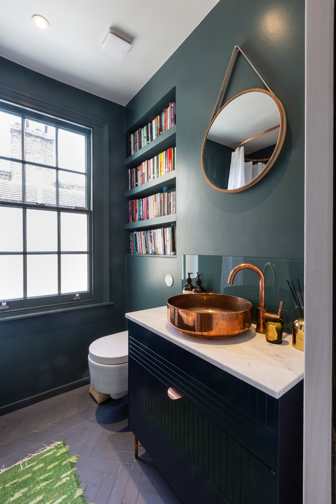 This is an example of a contemporary cloakroom in London with flat-panel cabinets, black cabinets, a wall mounted toilet, green walls, dark hardwood flooring, a vessel sink, brown floors and white worktops.