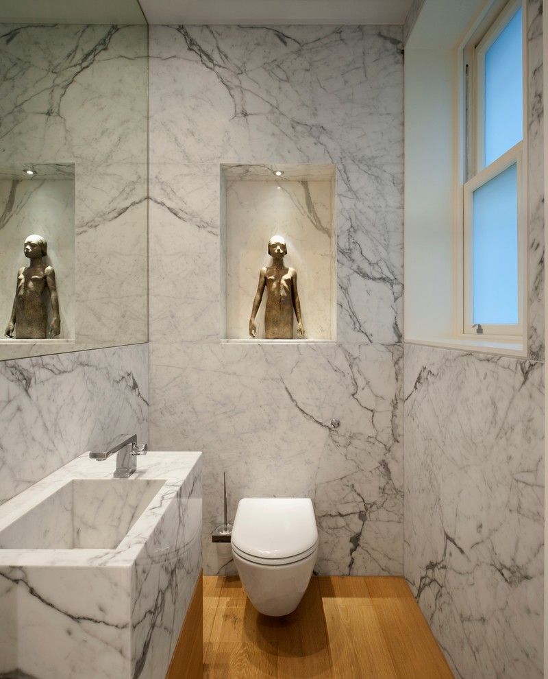 Modern inredning av ett litet toalett, med ett integrerad handfat, en vägghängd toalettstol, mellanmörkt trägolv, marmorbänkskiva, grå väggar och marmorkakel