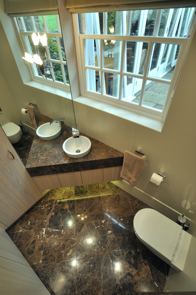 Inredning av ett modernt litet brun brunt toalett, med släta luckor, skåp i ljust trä, en vägghängd toalettstol, beige kakel, beige väggar, marmorgolv, ett integrerad handfat, marmorbänkskiva och brunt golv