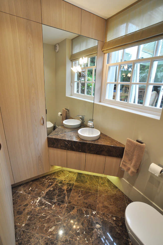 Esempio di un piccolo bagno di servizio minimal con ante lisce, ante in legno chiaro, WC sospeso, piastrelle beige, pareti beige, pavimento in marmo, lavabo integrato, top in marmo, pavimento marrone e top marrone