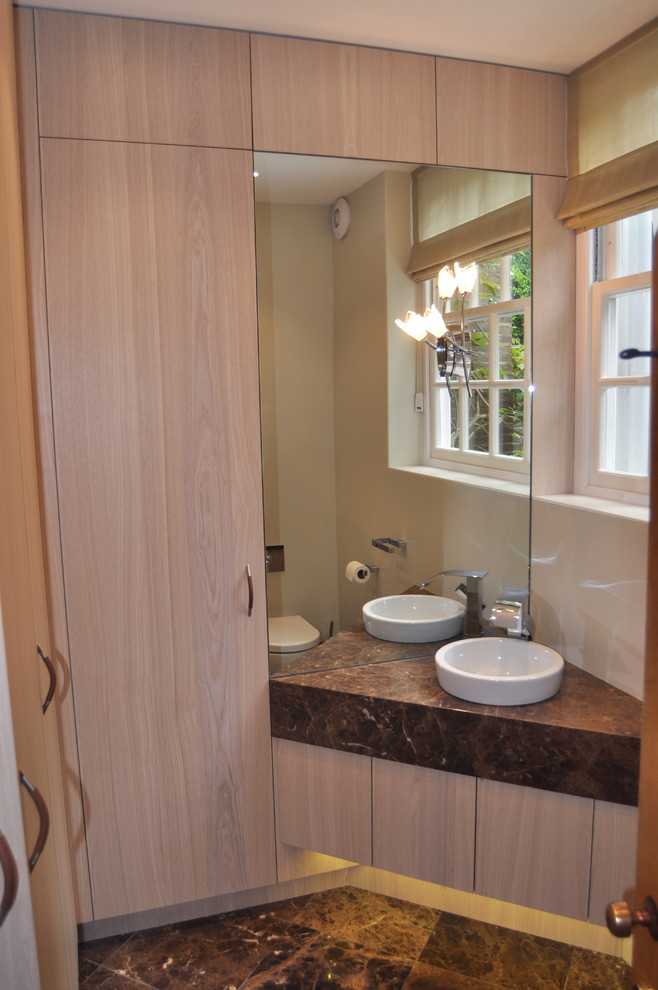 Réalisation d'un petit WC suspendu design en bois clair avec un placard à porte plane, un carrelage beige, un mur beige, un sol en marbre, un lavabo intégré, un plan de toilette en marbre, un sol marron et un plan de toilette marron.