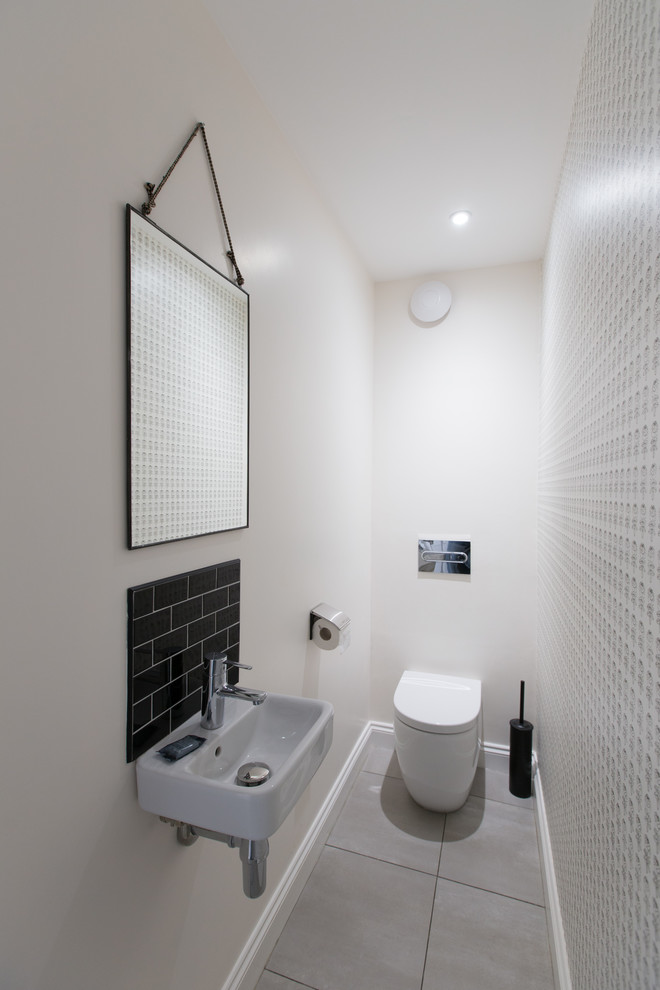 Small scandi cloakroom in Wiltshire with a one-piece toilet, black tiles, ceramic tiles, white walls, lino flooring and a wall-mounted sink.