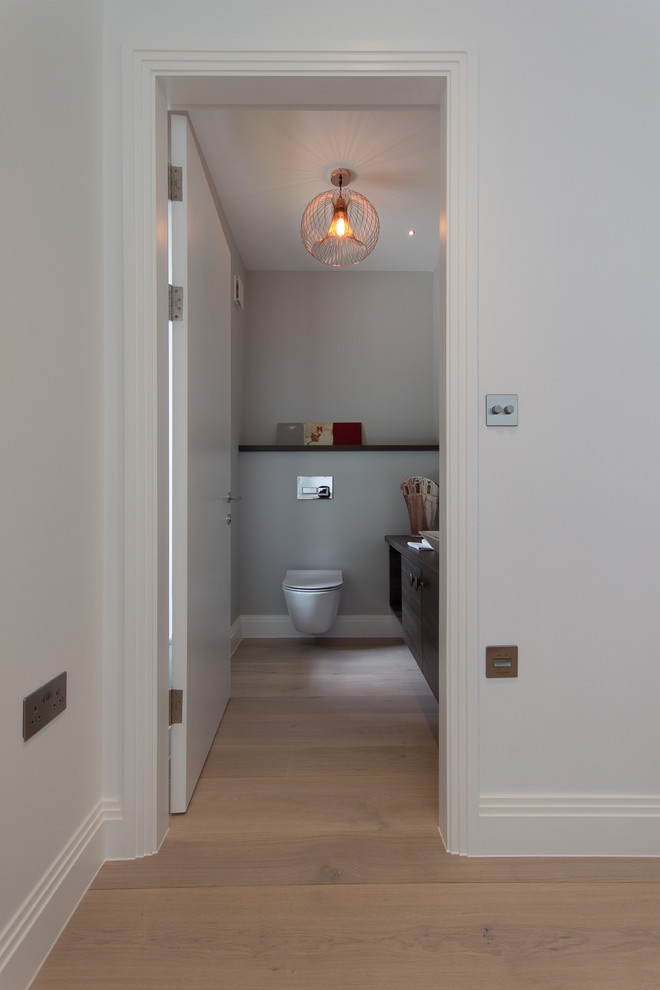 This is an example of a medium sized modern cloakroom in London with flat-panel cabinets, dark wood cabinets, a wall mounted toilet, grey walls, medium hardwood flooring, a console sink, wooden worktops and brown floors.