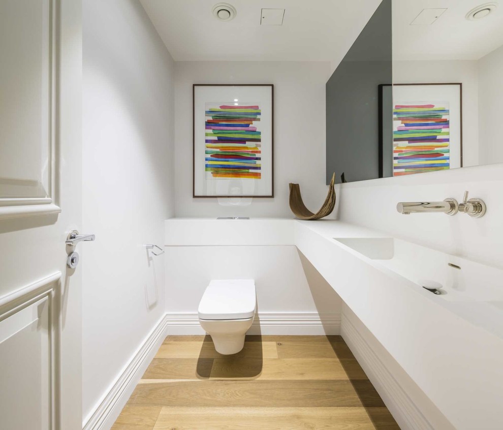 Cette photo montre un petit WC suspendu tendance avec des portes de placard blanches, un mur blanc, un sol en bois brun, un lavabo posé, un plan de toilette en surface solide, un plan de toilette blanc et meuble-lavabo encastré.